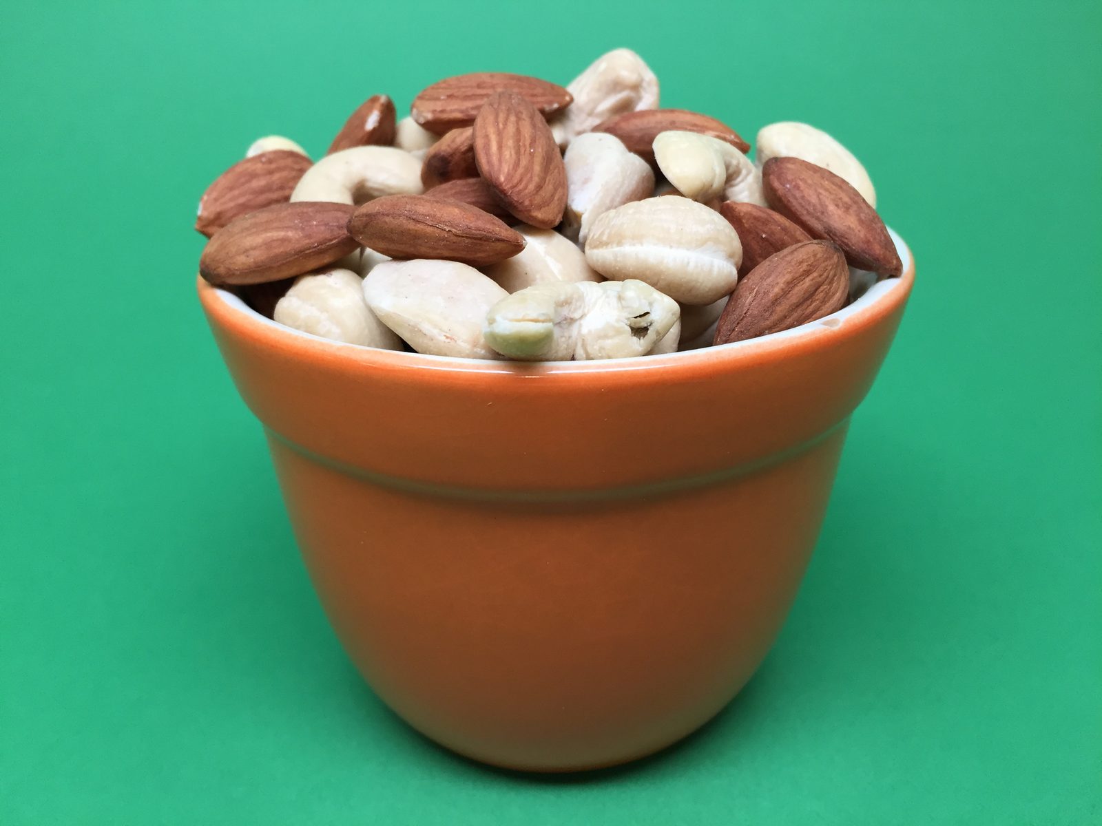 A wooden bowl filled with raw almonds and cashews