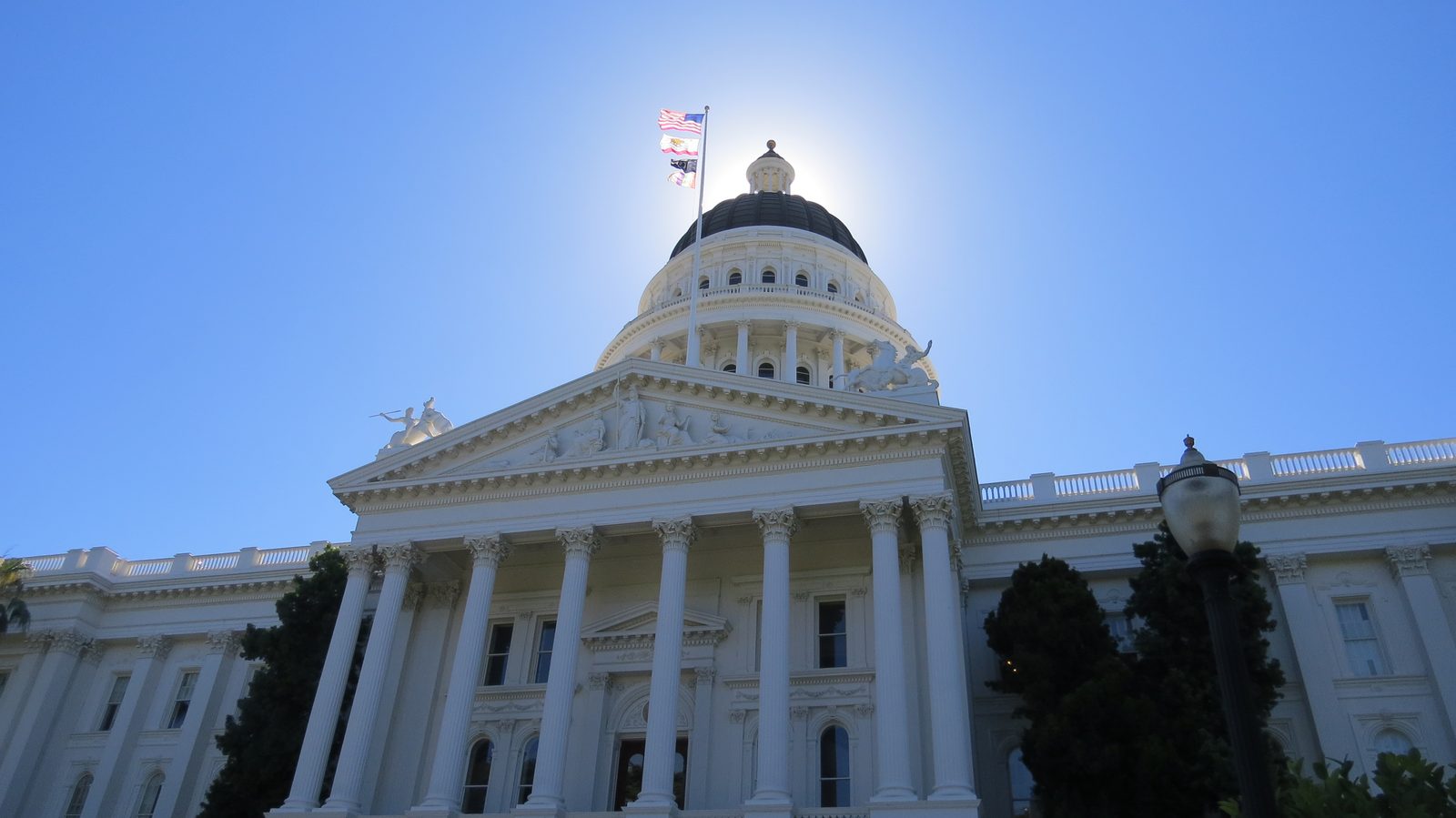 A white columned portico and dome backlit by the sun against a clear blue sky