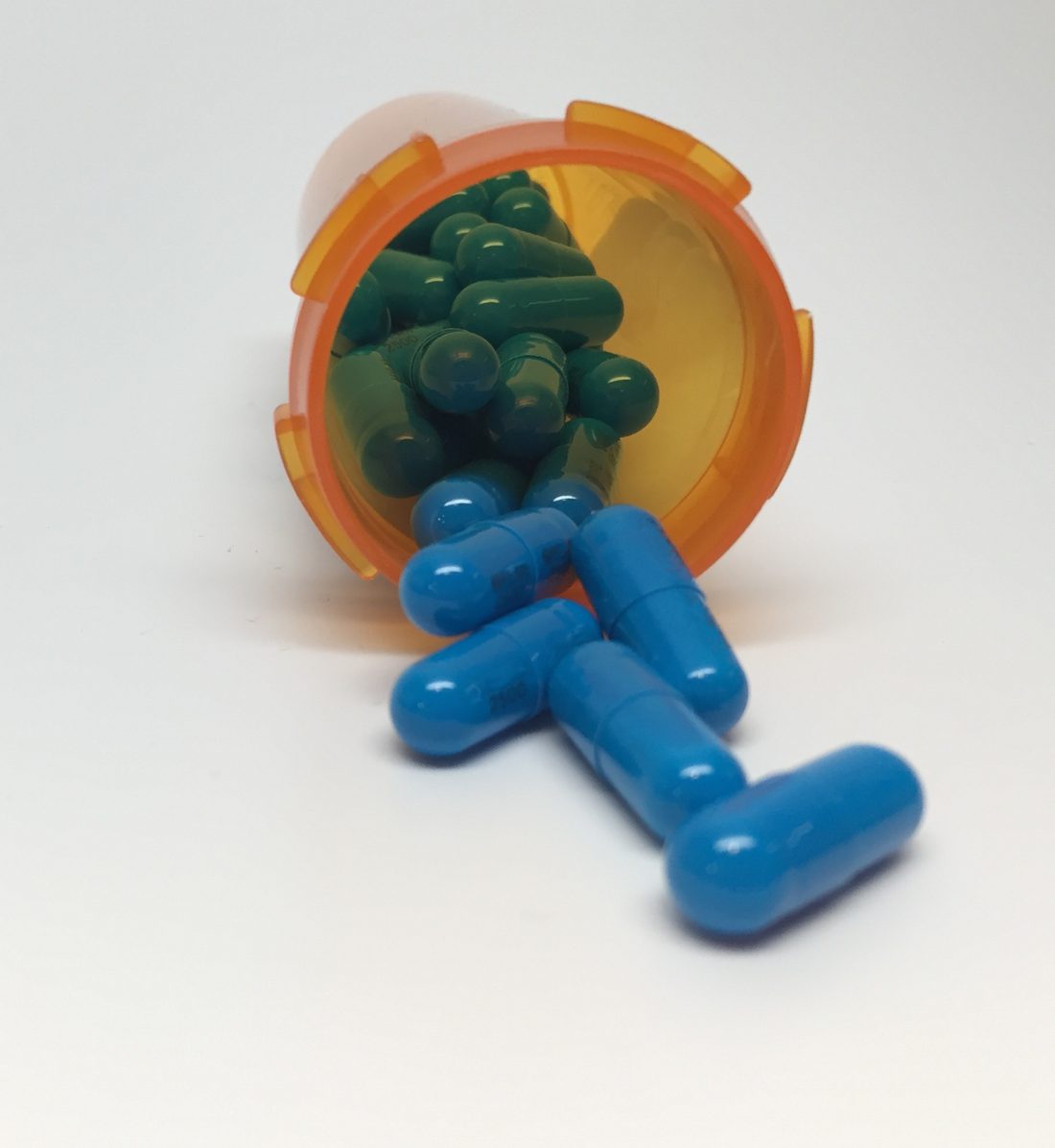 Capsules spilling out of an open prescription pill bottle onto a plain surface