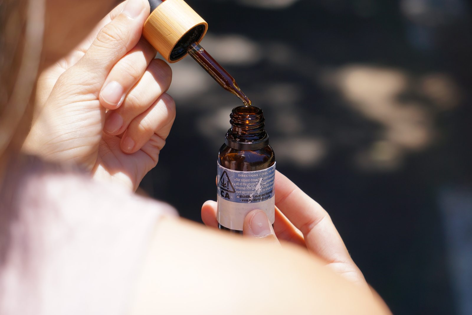 A person holds a dropper of CBD oil above the open bottle