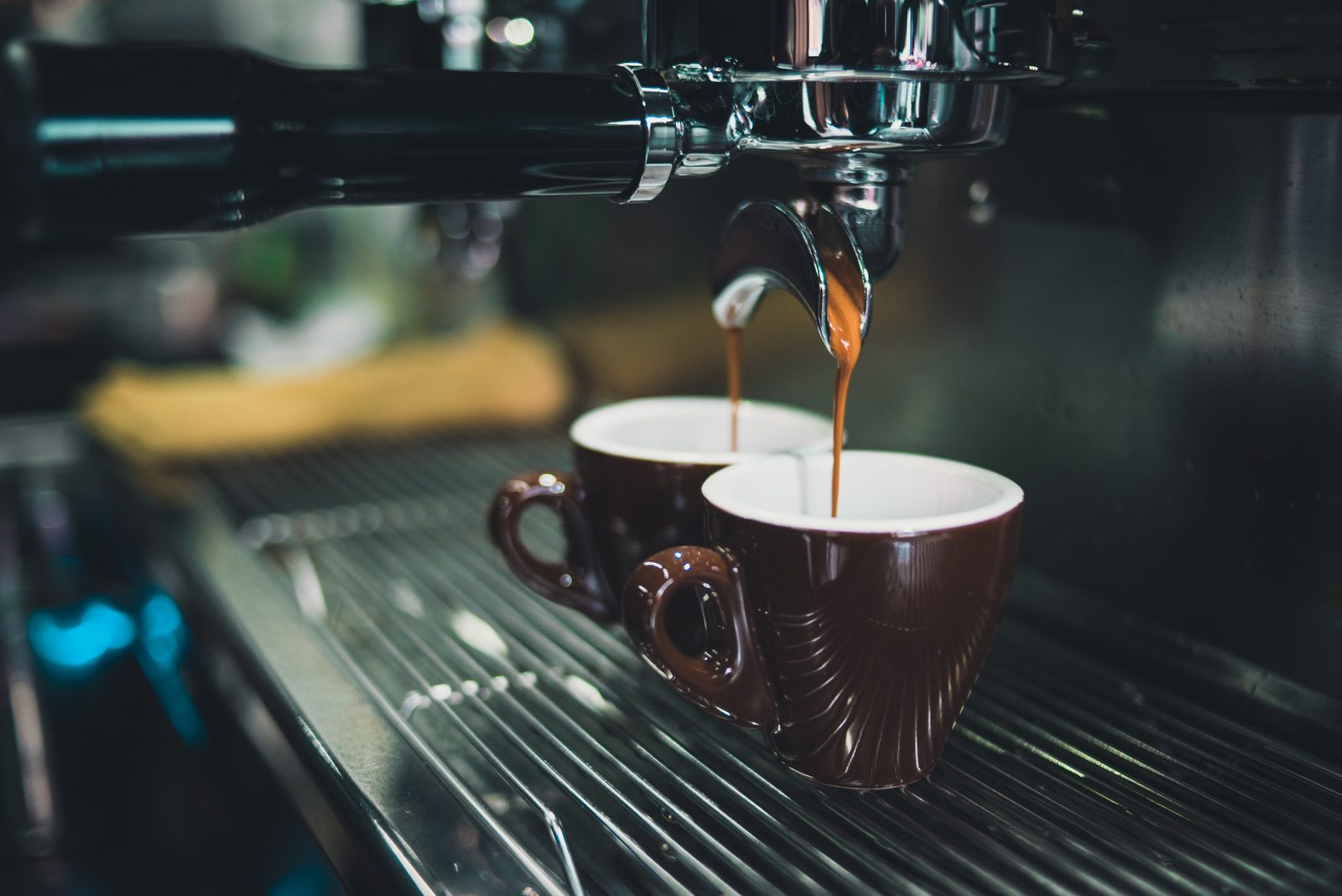 Two brown coffee cups filled under an espresso machine, photographed close up