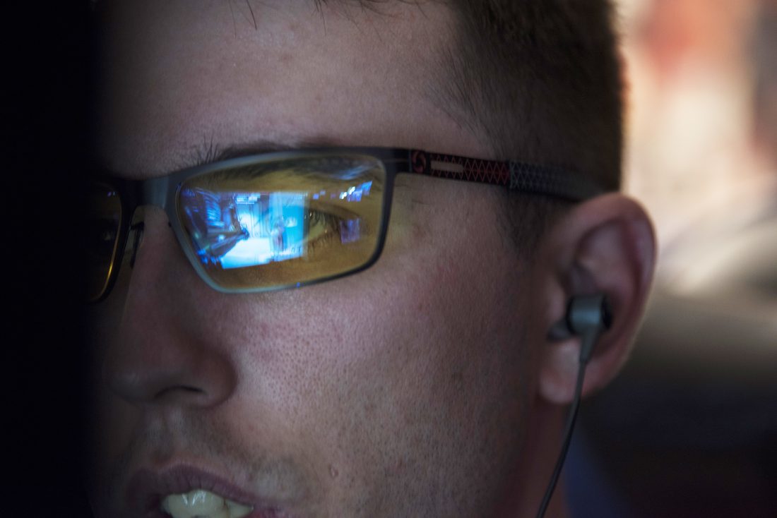 Close up of a competitive gamer's face in profile, a video game reflected in his glasses, jaw set in concentration during an esports tournament