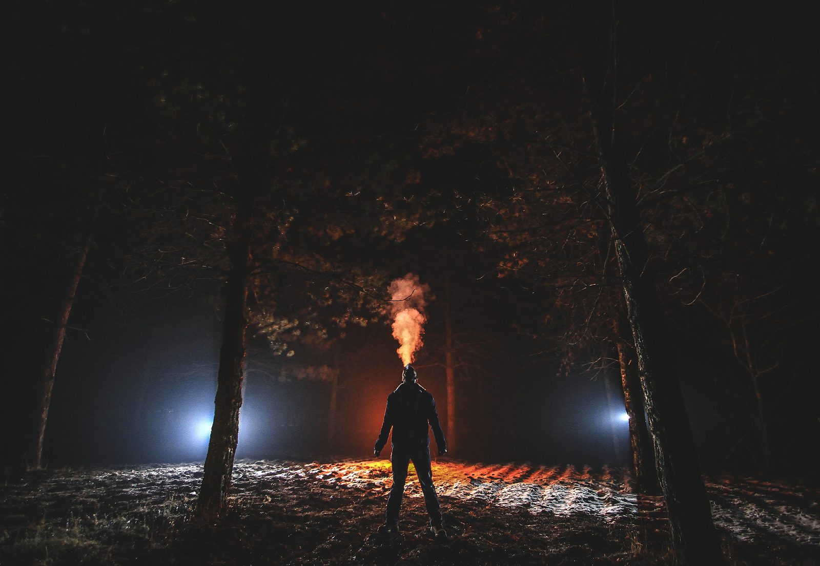 A person exhaling on a cold night, the breath lit from behind
