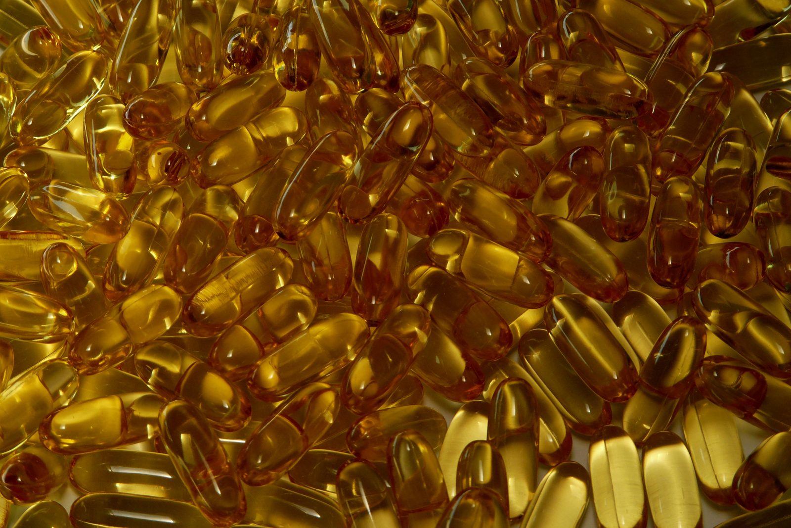 A loose pile of amber colored gelatin softgel capsules photographed close up