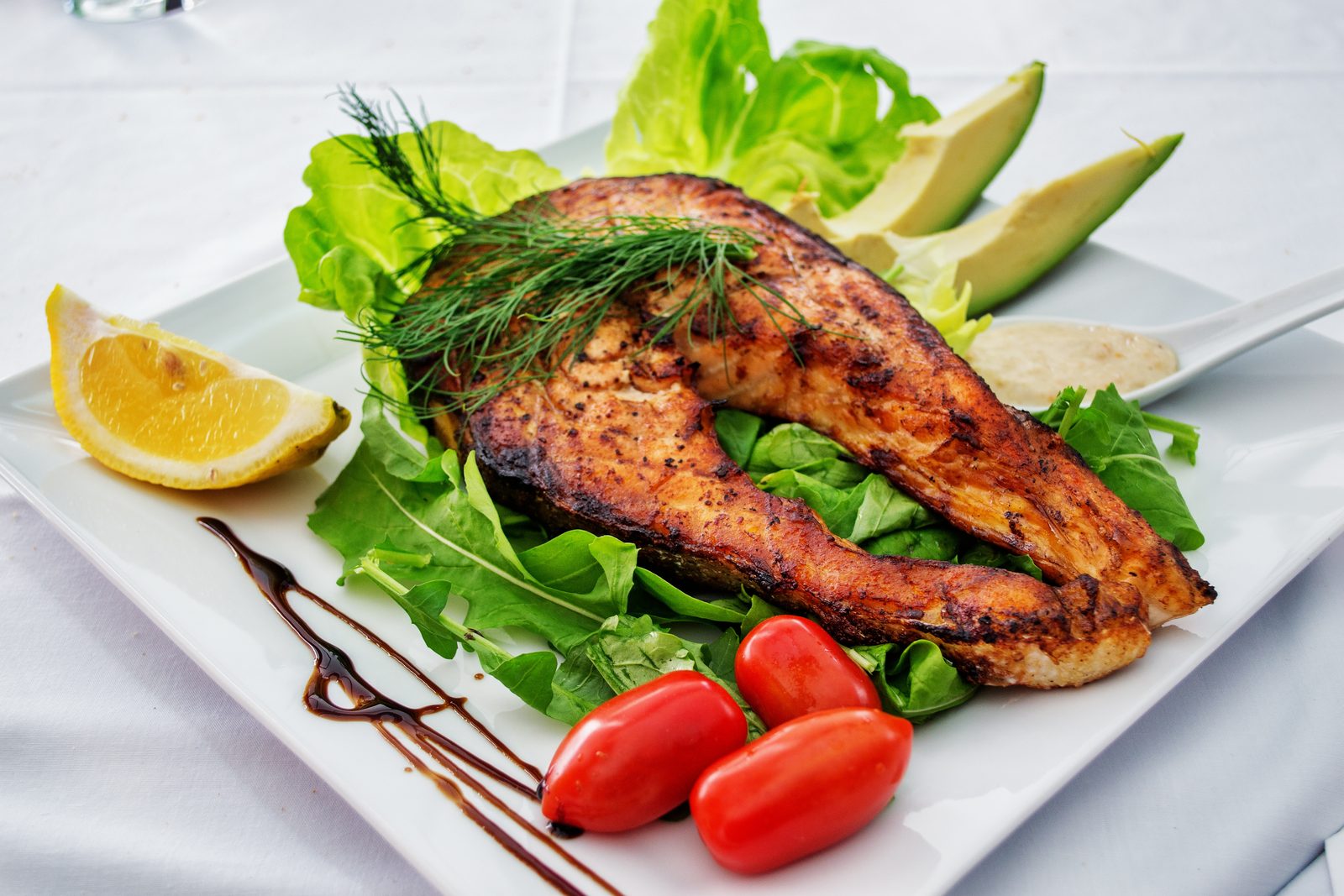 A grilled salmon fillet on a plate, photographed against a plain background