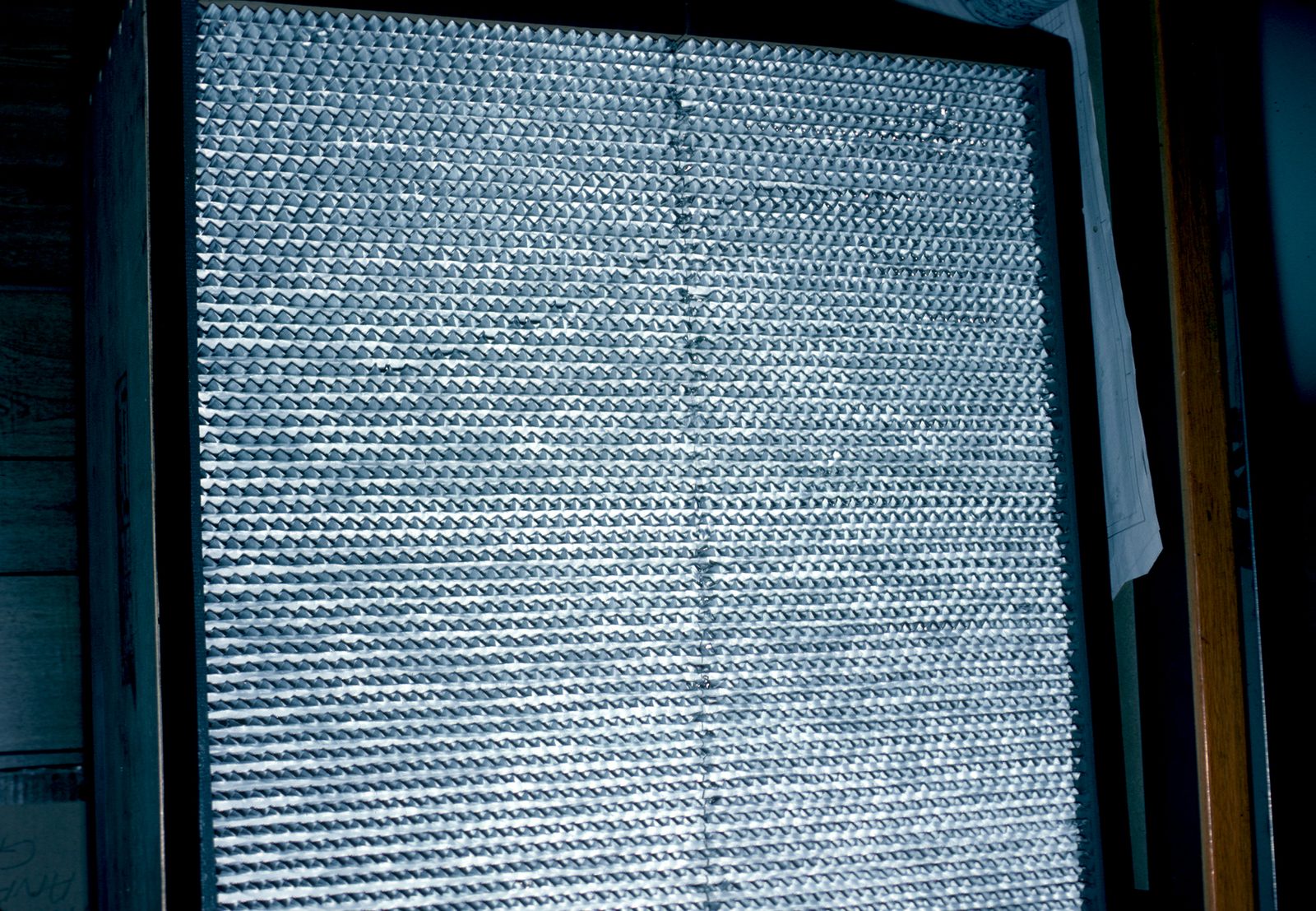 A close up, backlit photograph of a HEPA filter's pleated white media, showing the fine repeating fold pattern that traps airborne particles