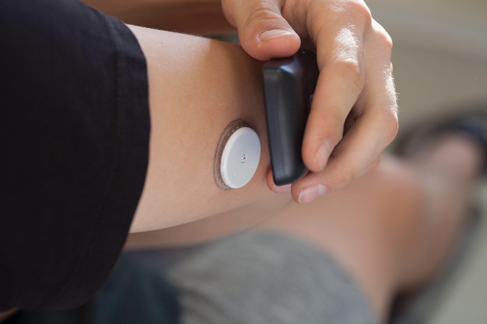 Close up of an Abbott FreeStyle Libre glucose sensor worn on the upper arm, being read by its handheld scanner