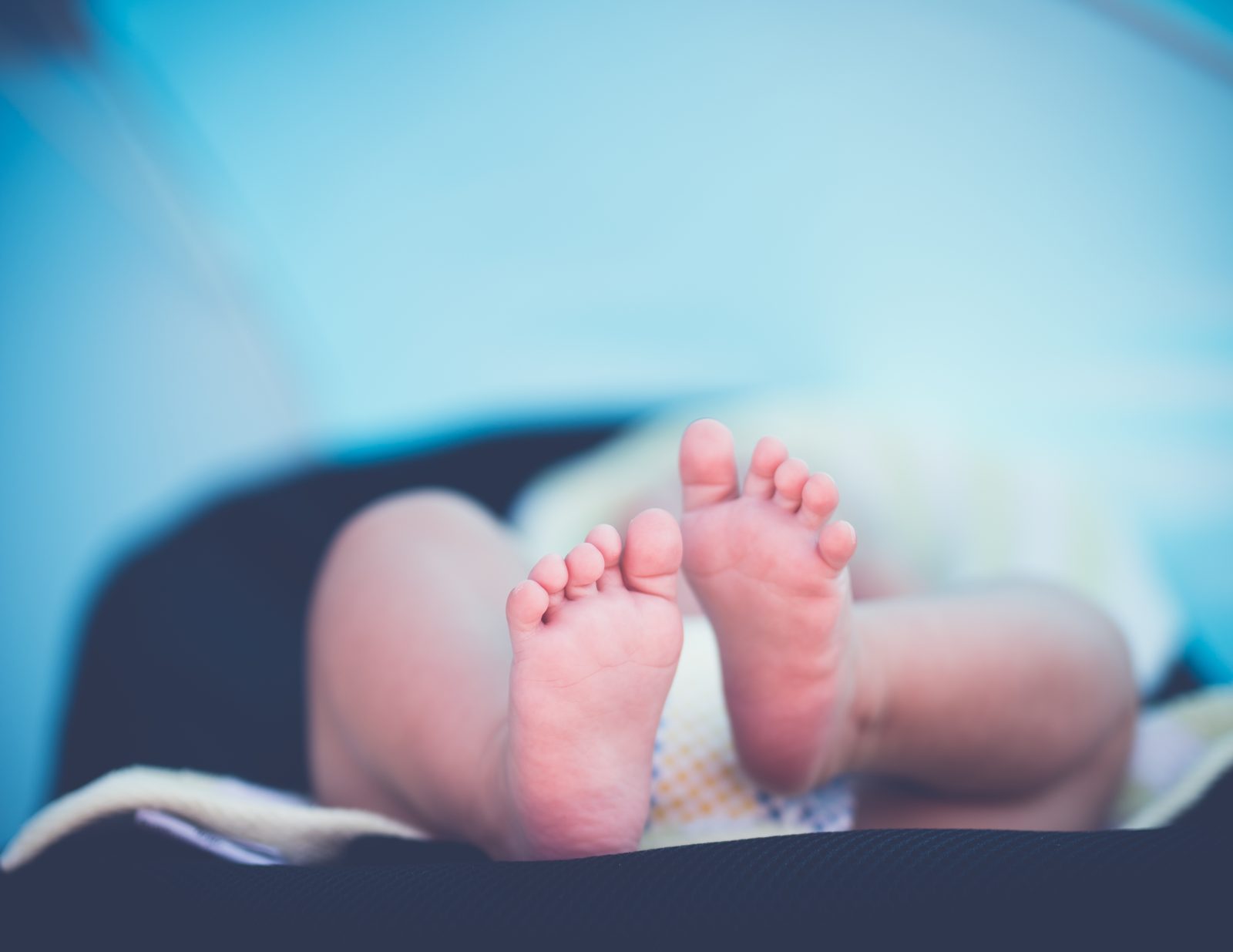 Close up of a newborn baby's bare feet, soft focus, against a pale blue background
