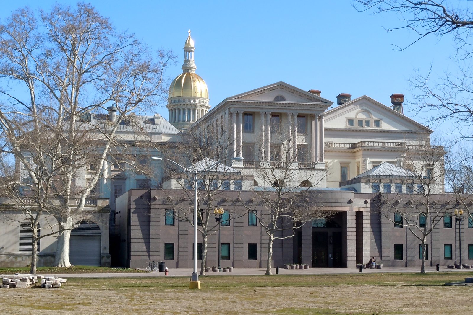 The New Jersey State House in Trenton, a stone building with a gold dome, photographed from across the lawn on a clear day