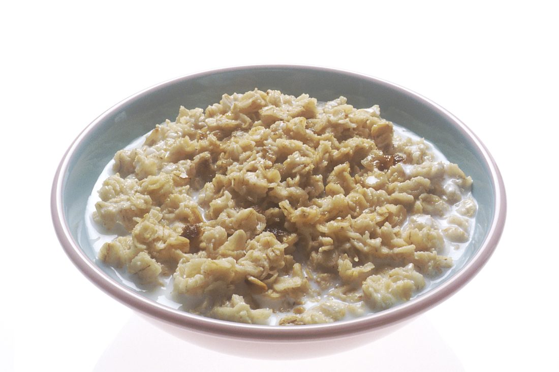 A single white bowl of cooked oatmeal with milk, photographed against a plain white background