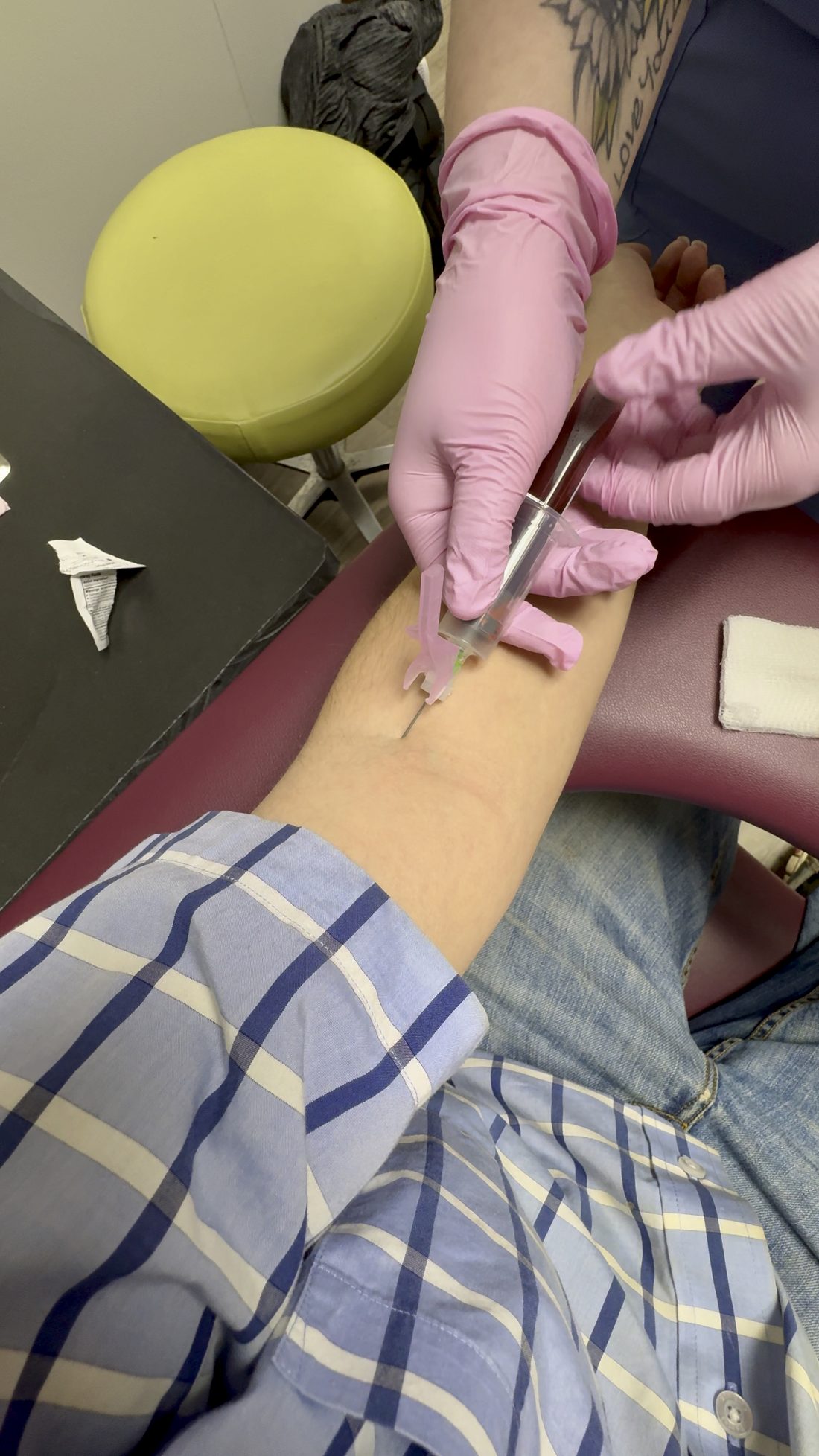 A gloved clinician draws blood from a patient's arm with a syringe during a routine blood draw
