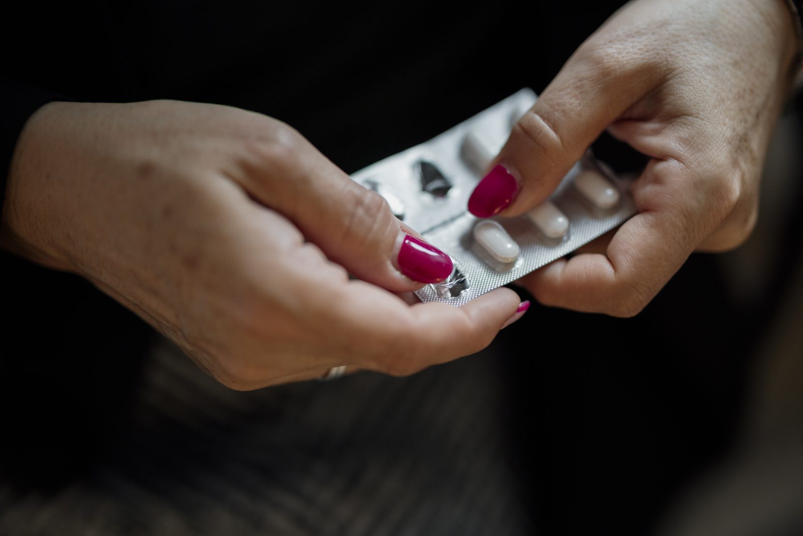Two hands holding a blister pack and pressing a tablet out of it