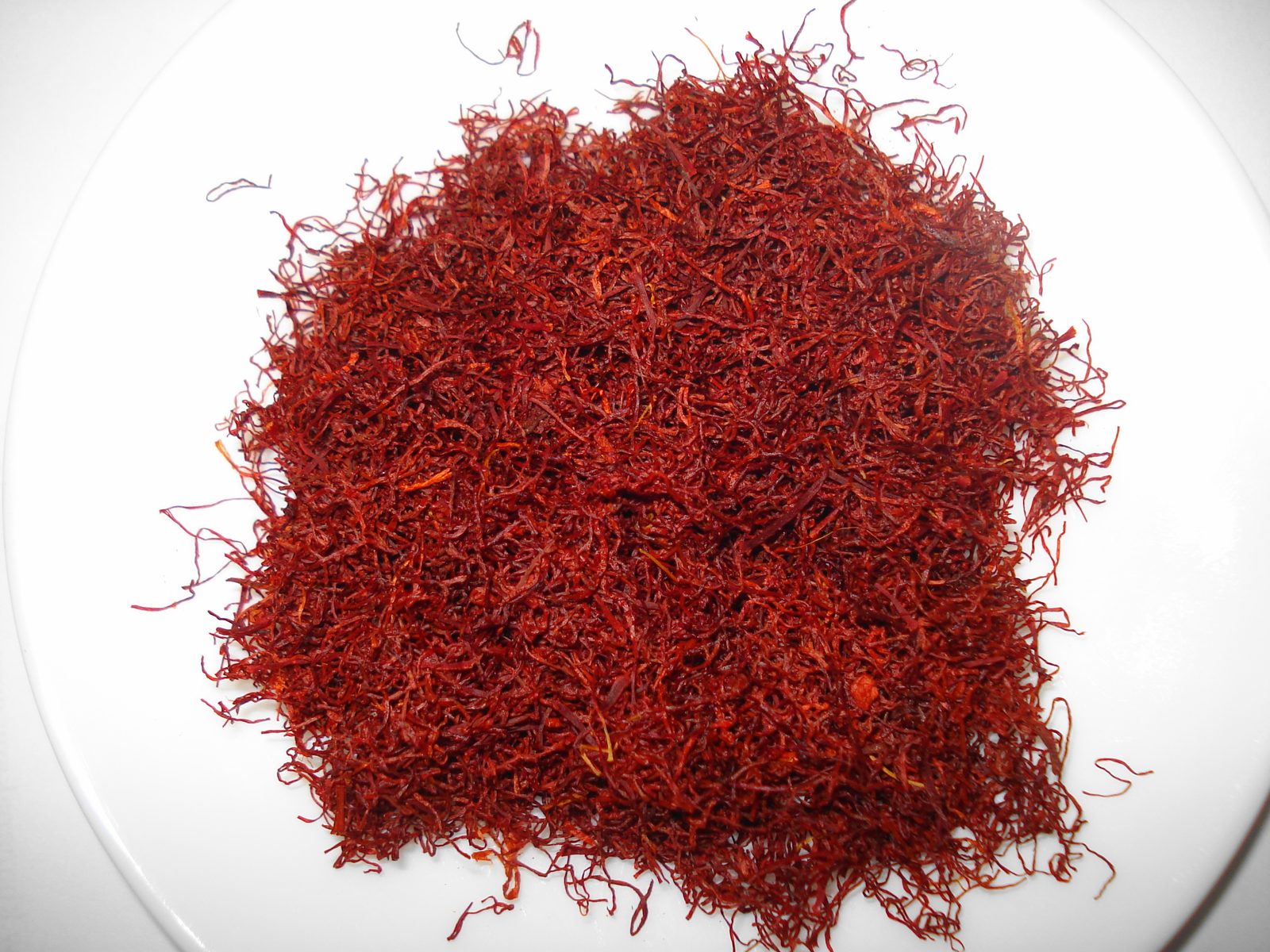A pile of dried red saffron threads on a plain white plate, photographed from above