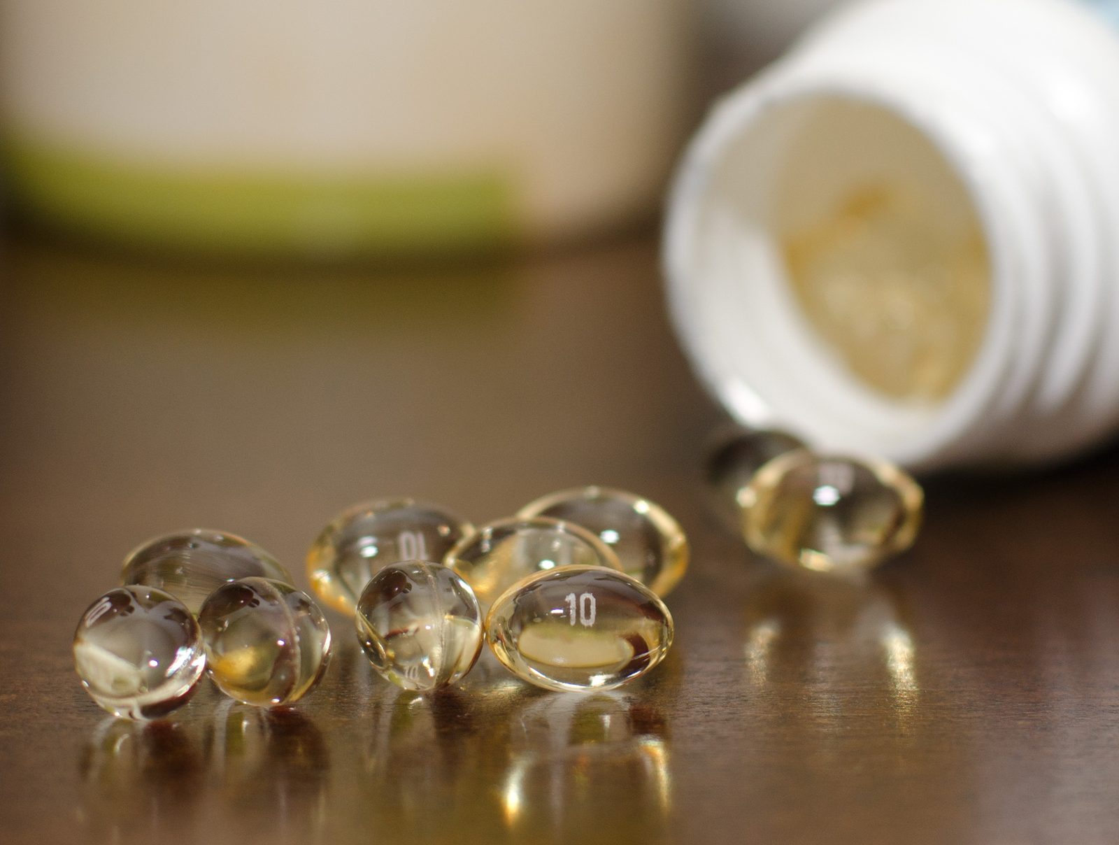 Clear oil softgel capsules on a dark wooden table, with the white bottle they spilled from out of focus behind them